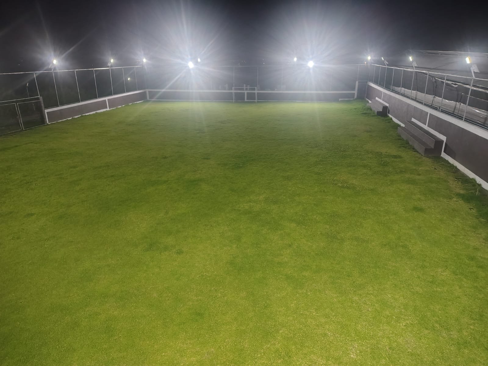 Vista panorámica nocturna de un campo de fútbol de césped sintético.